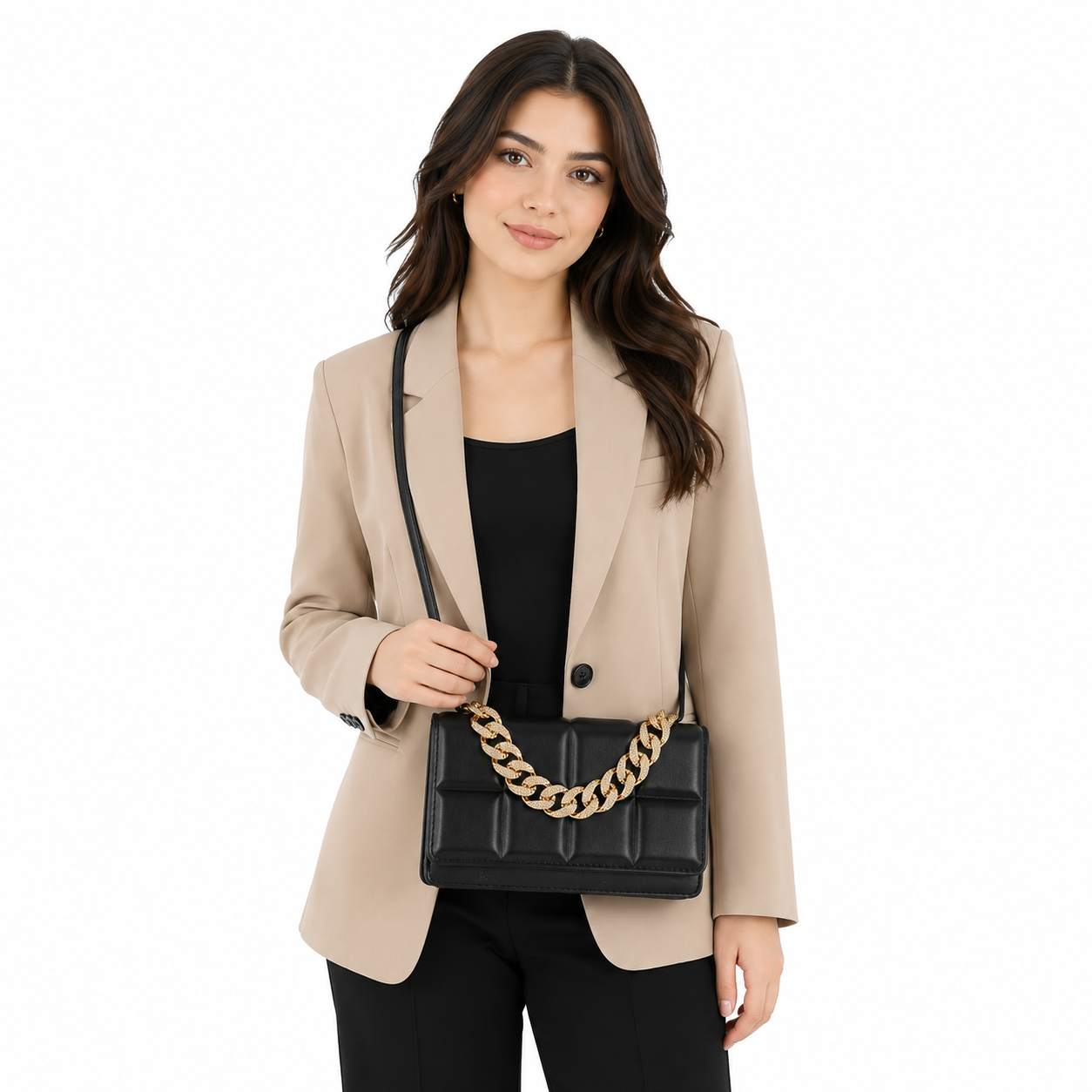 A woman wearing a beige blazer, black top, and black pants carries a black quilted crossbody bag with a gold chain strap against a plain white background.