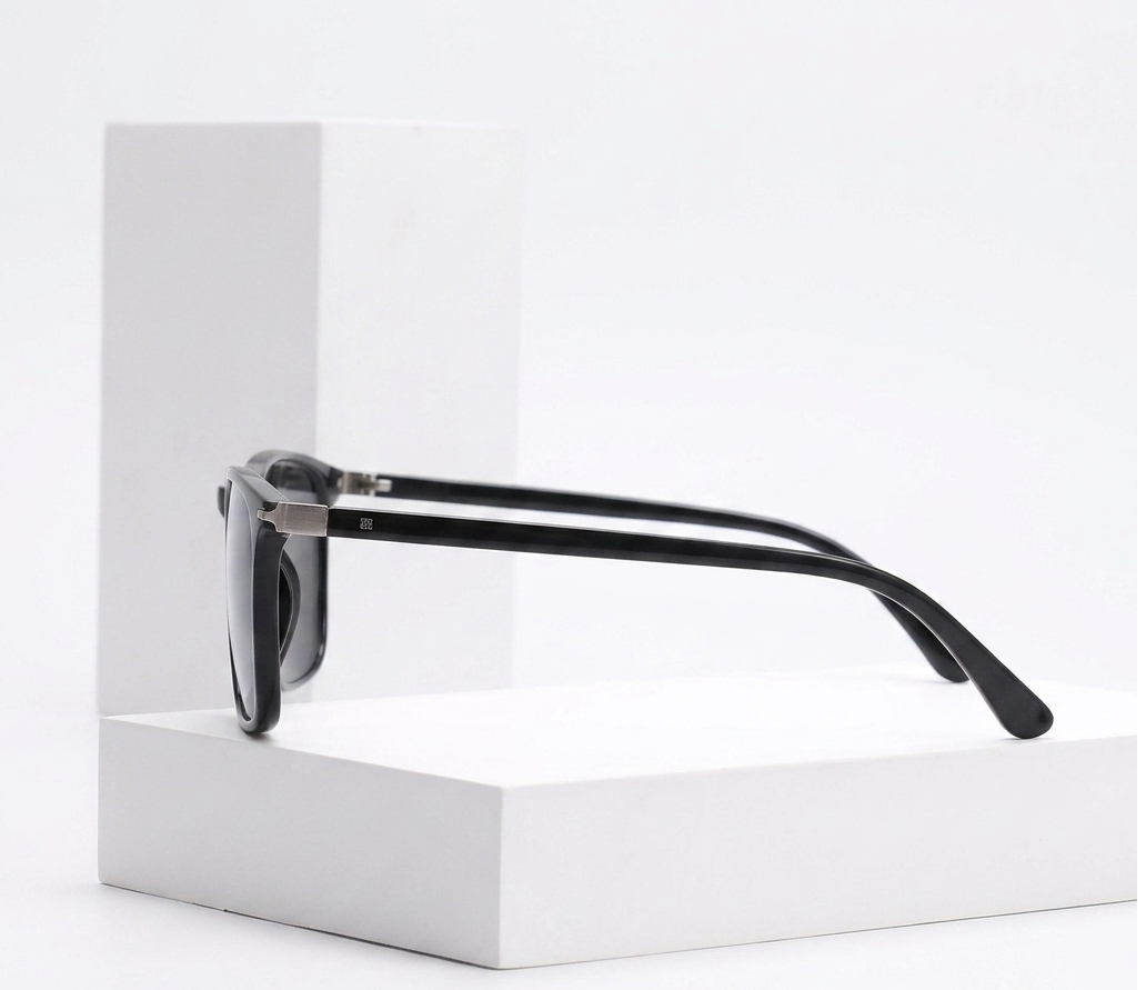 Black sunglasses with silver metal hinges, displayed on a white geometric pedestal against a clean white background.