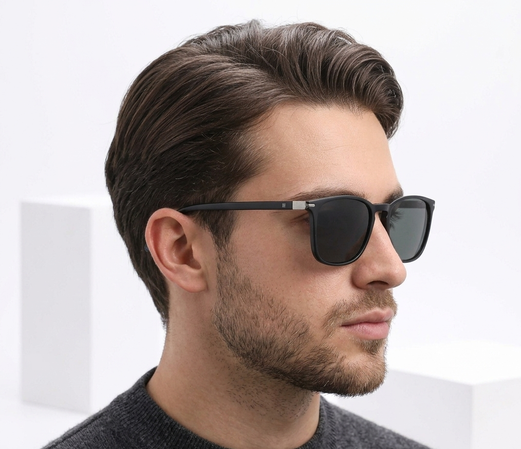 A man in profile wearing black square sunglasses with dark lenses, shown against a clean white studio background with geometric blocks.