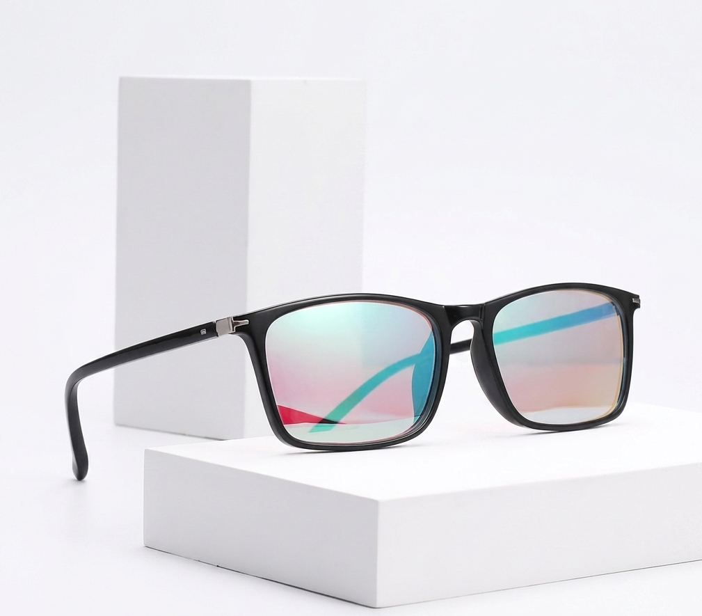 Black square sunglasses with mirrored lenses showing a blue, pink, and green iridescent reflection, displayed on white geometric blocks against a white background.