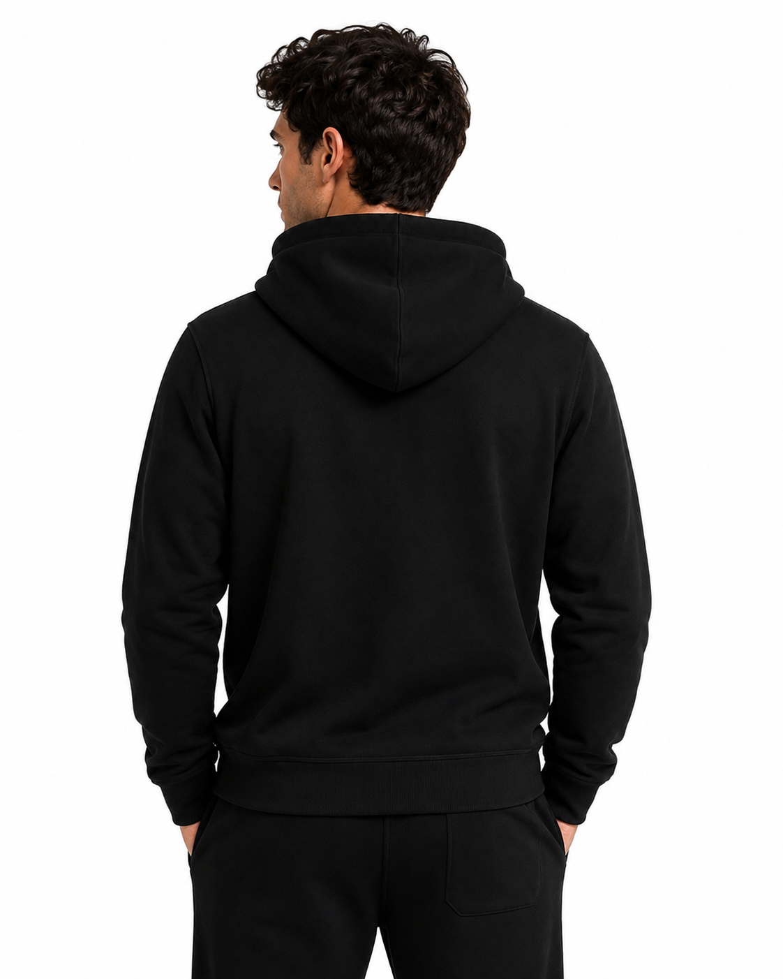 A man viewed from the back wearing a plain black pullover hoodie and black pants against a clean white studio background.